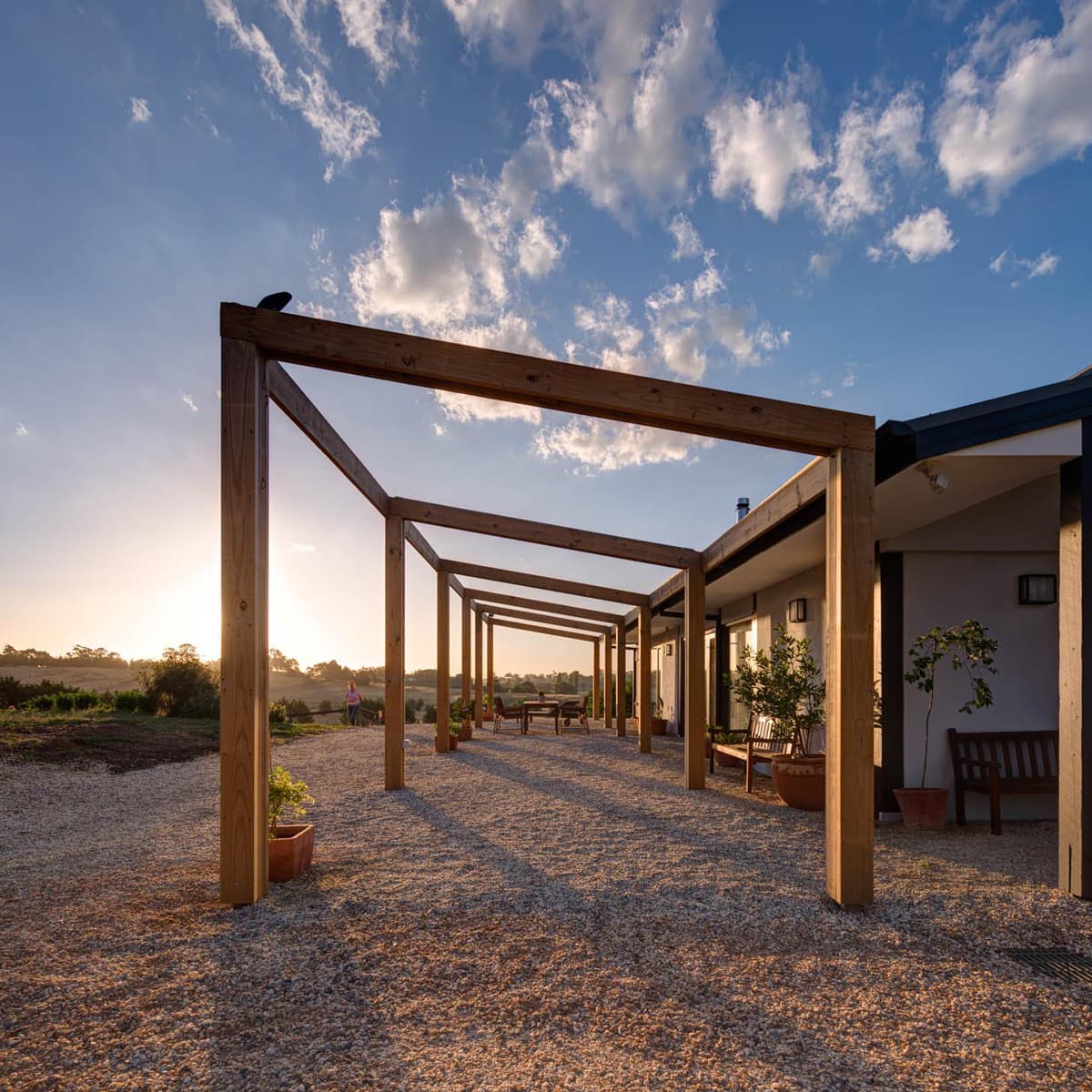 Timber pergola over a gravel courtyard beside the house at sunset